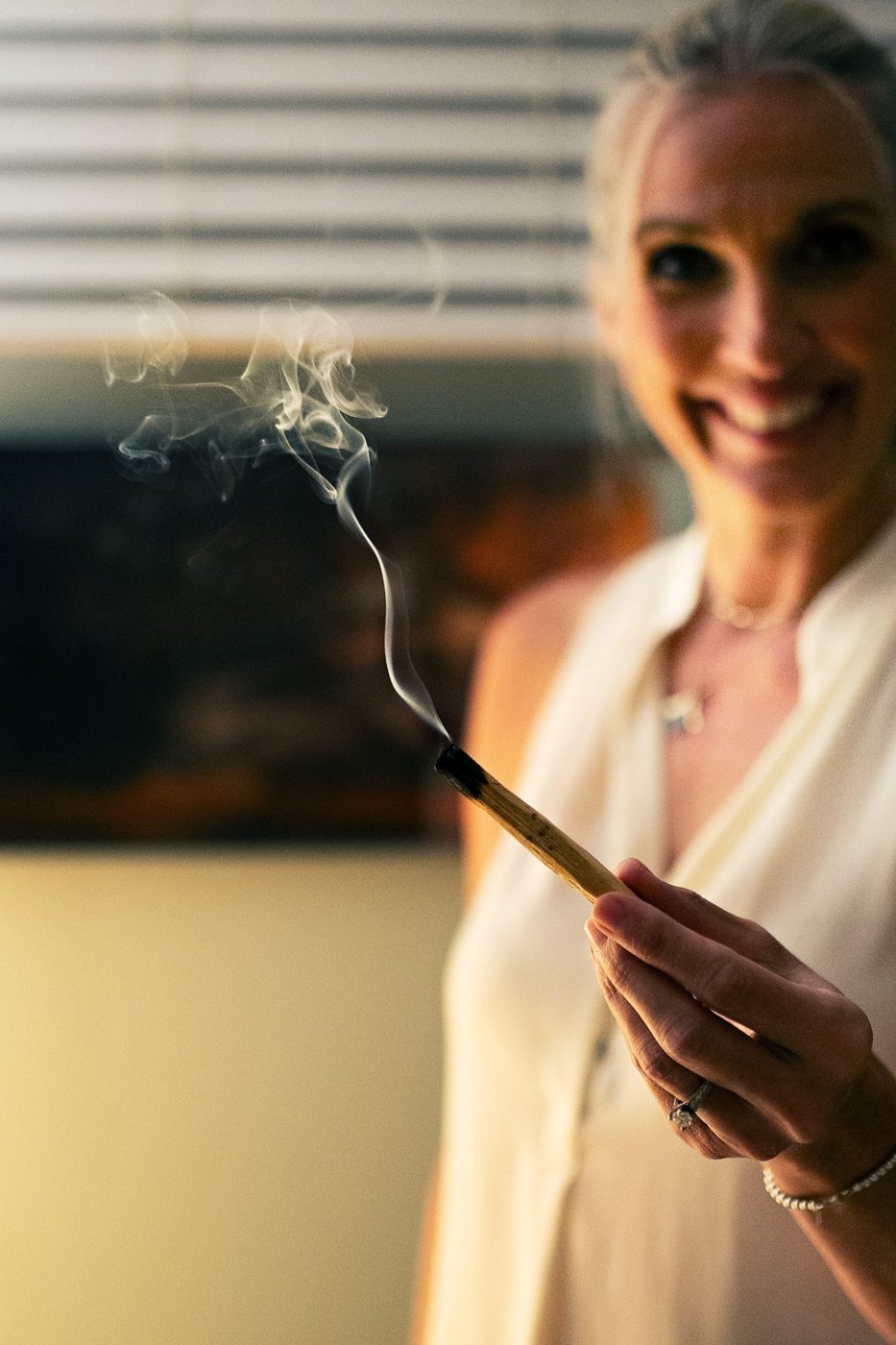 Tami Watson smiling, holding a smoking stick of palo santo