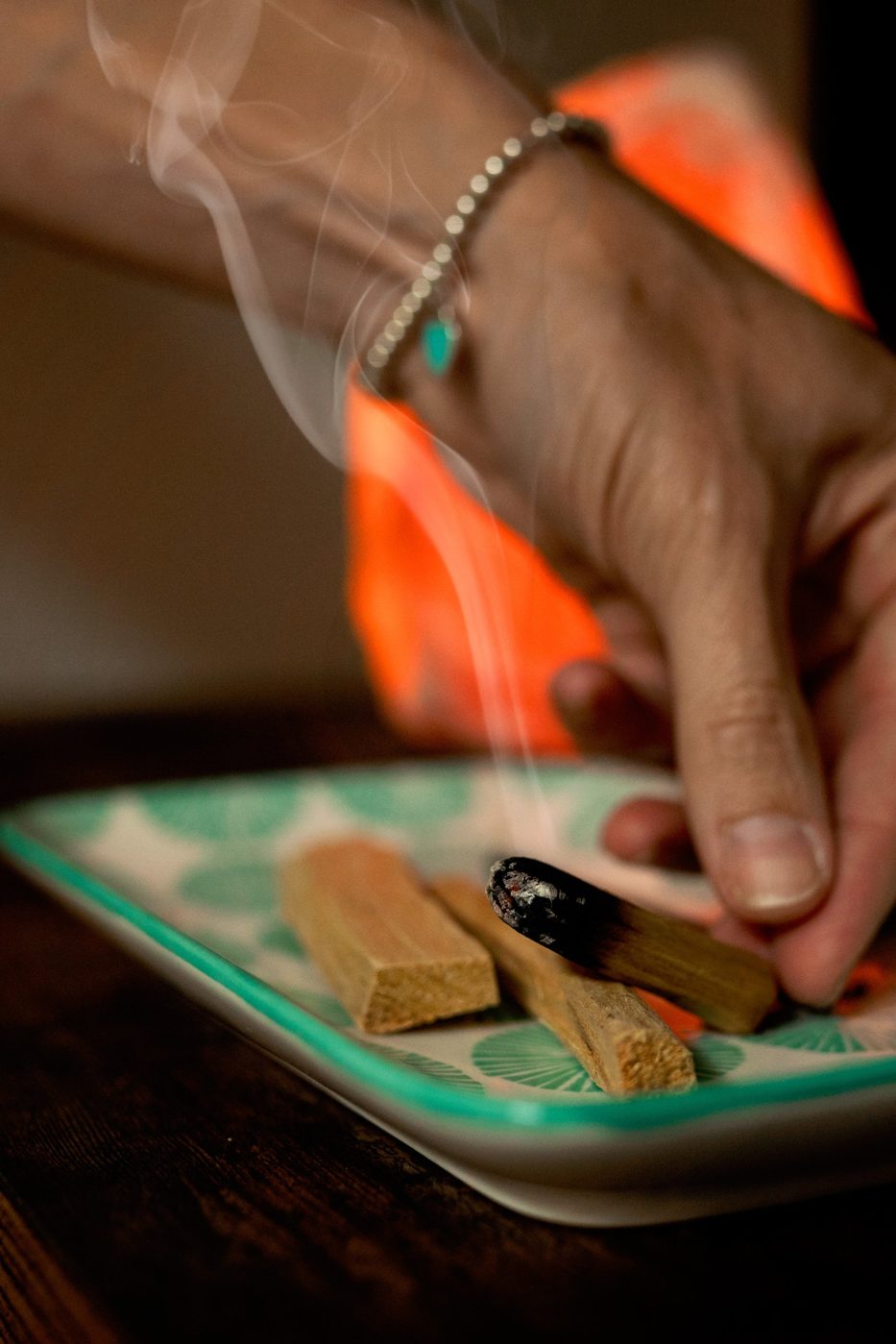 Tami’s hand setting a smoldering stick of palo santo on a ceramic tray