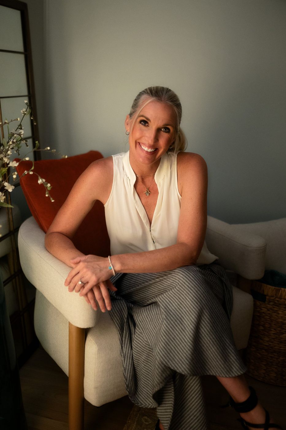 Tami Watson smiling, seated in an armchair in her Millcreek studio